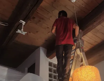 Operatore su scala esegue trattamento antitarlo a irrorazione e pennello su travi in legno interne.